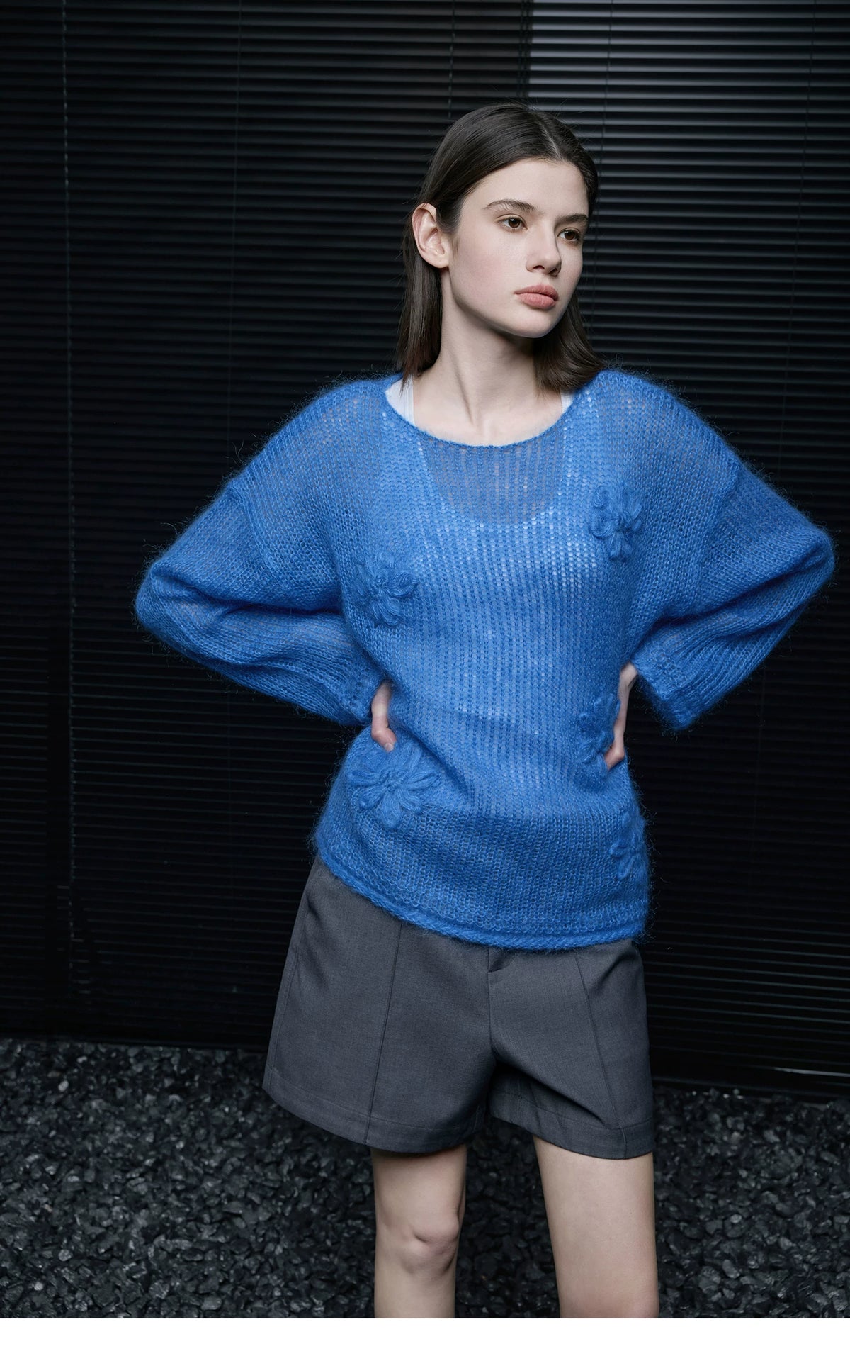 Model in Cobalt Blue semi-sheer floral knit pullover with hands on hips, paired with grey tailored shorts
