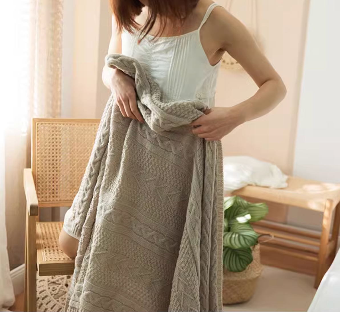 Woman wrapped in light gray braided knit oversized throw blanket showing detailed cable knit texture and soft material