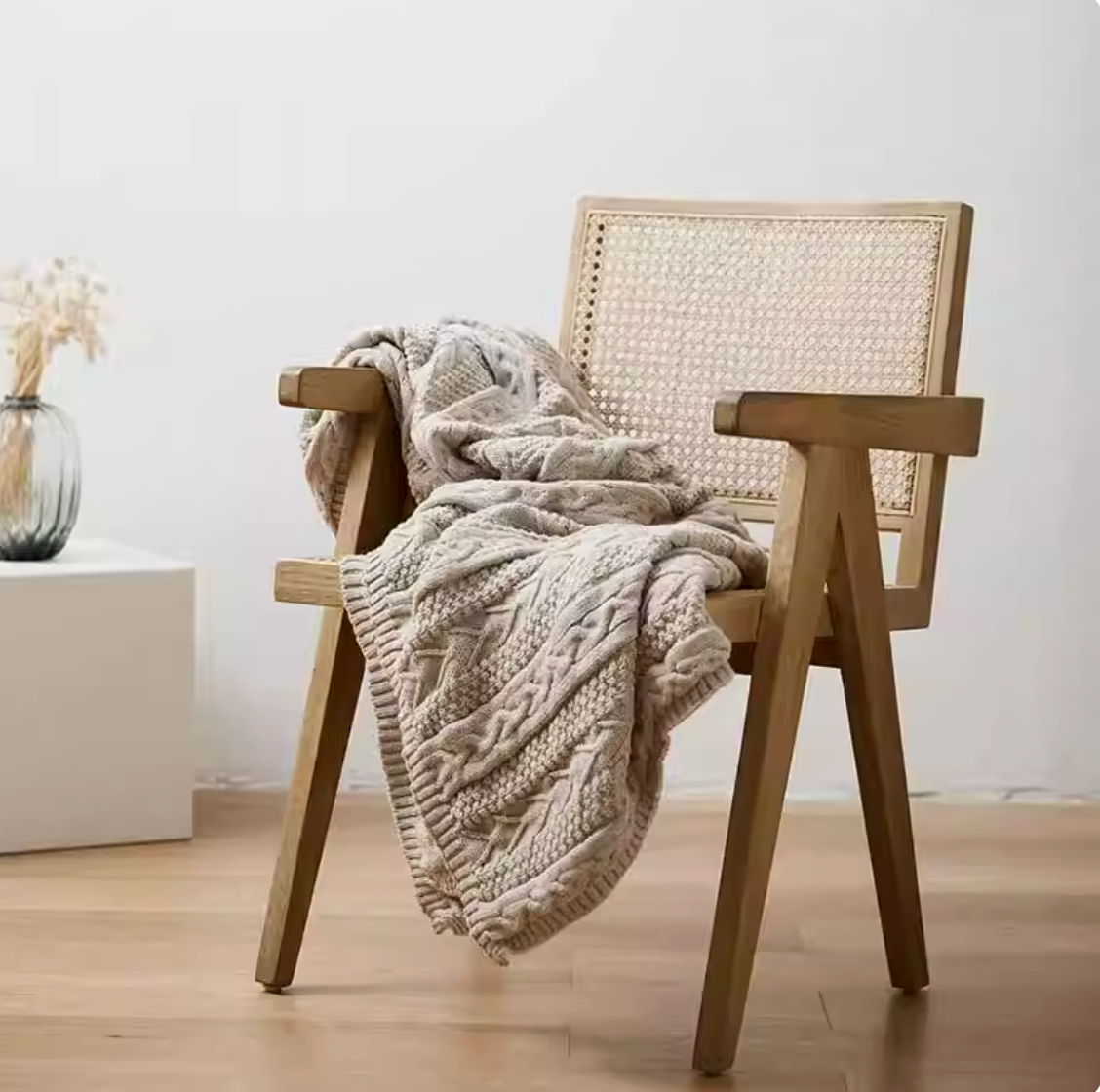 Light gray braided knit oversized throw blanket draped over wooden chair in a clean minimal interior setting