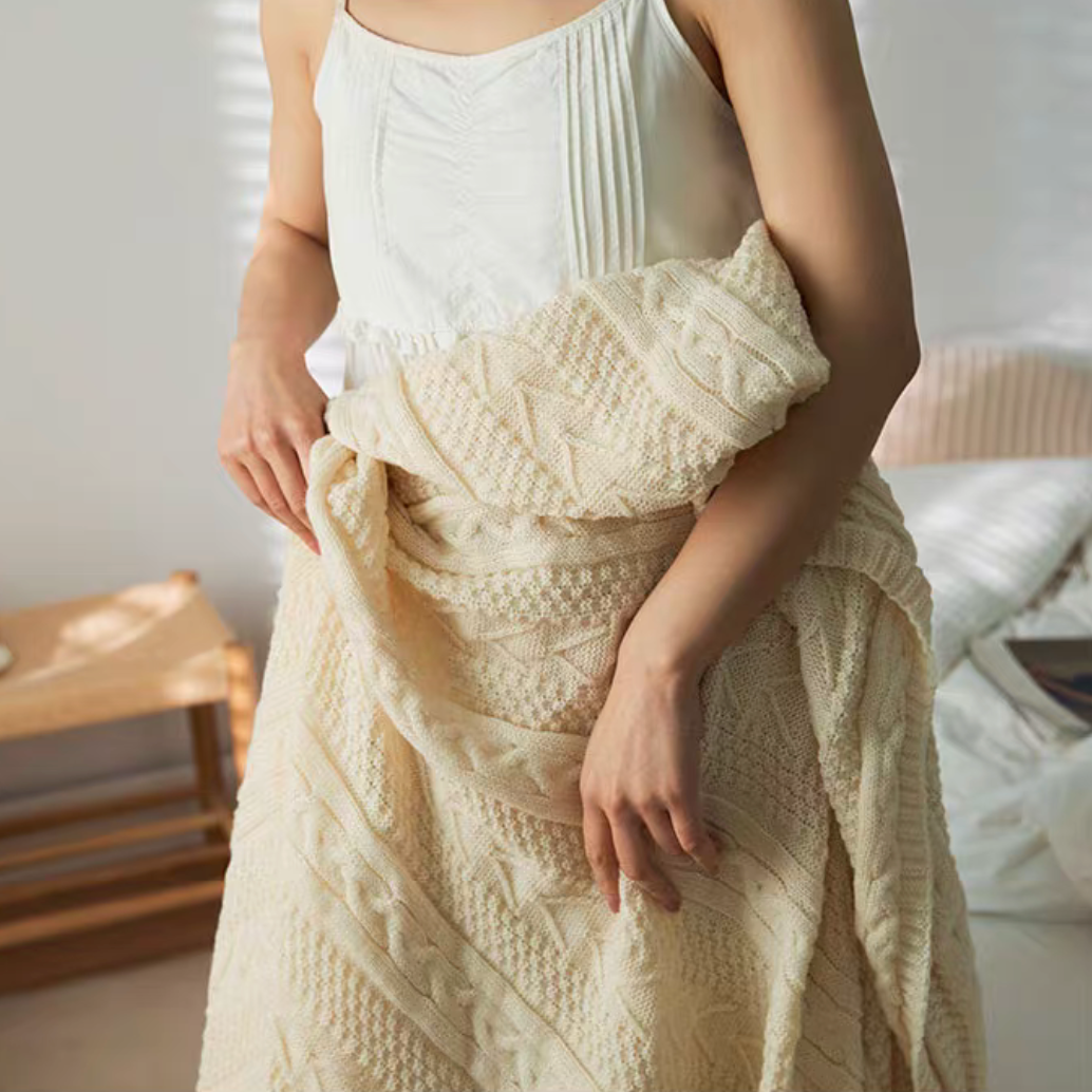 Close-up of white braided knit oversized throw blanket wrapped around body highlighting thick knit pattern and softness