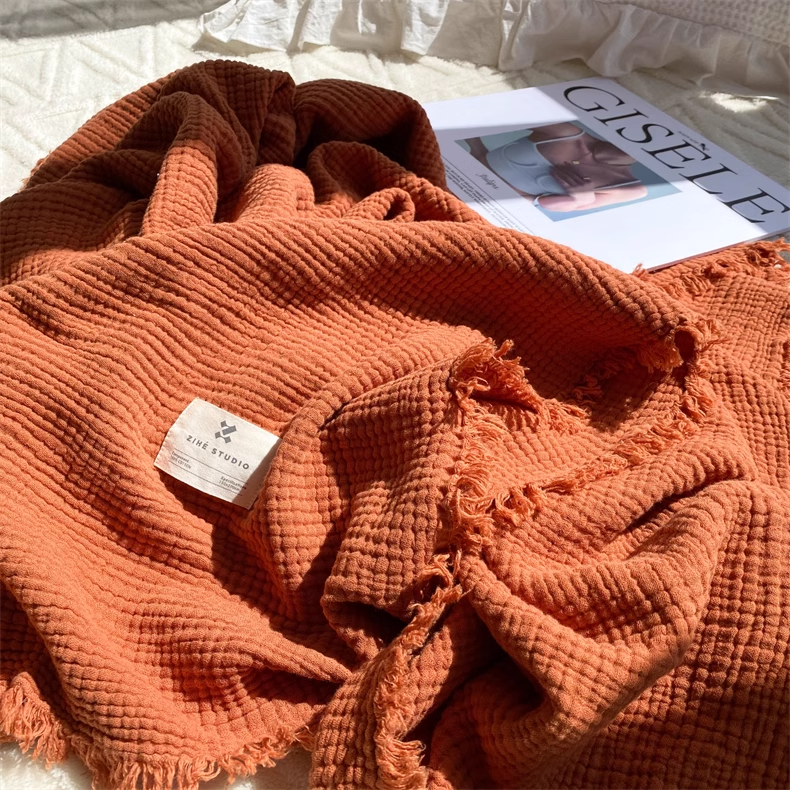 Caramel waffle textured organic cotton throw blanket with raw fringe edges displayed on bed with magazine styling.