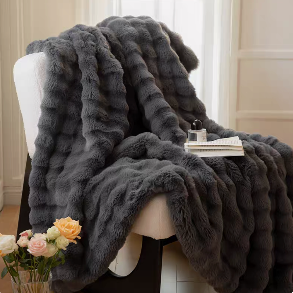Dark gray plush faux fur blanket on accent chair with flowers and book, thick soft sculpted cozy texture