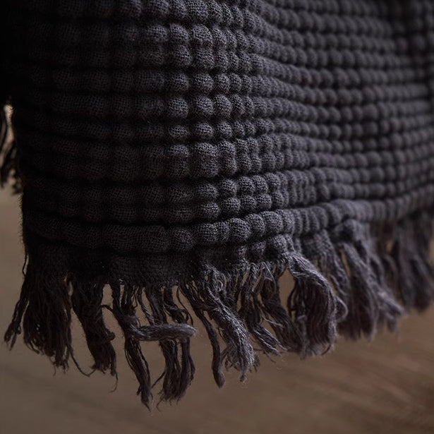 Deep charcoal gray organic cotton waffle gauze throw blanket close-up highlighting fringe edges and soft texture.