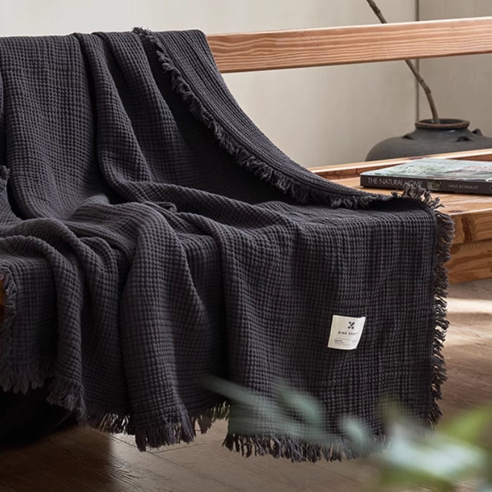 Deep charcoal gray waffle textured organic cotton fringe throw blanket draped elegantly over wooden chair.