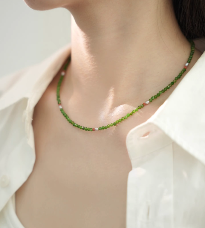 Close-up of model wearing emerald green gemstone necklace with diopside beads, freshwater pearl, and red agate accents