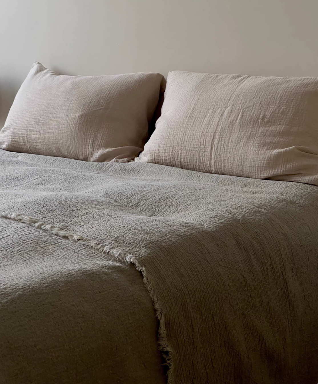 Close up of handcrafted raw edge fringe detail on classic natural French flax linen duvet thin quilt showing textured stonewashed linen fabric