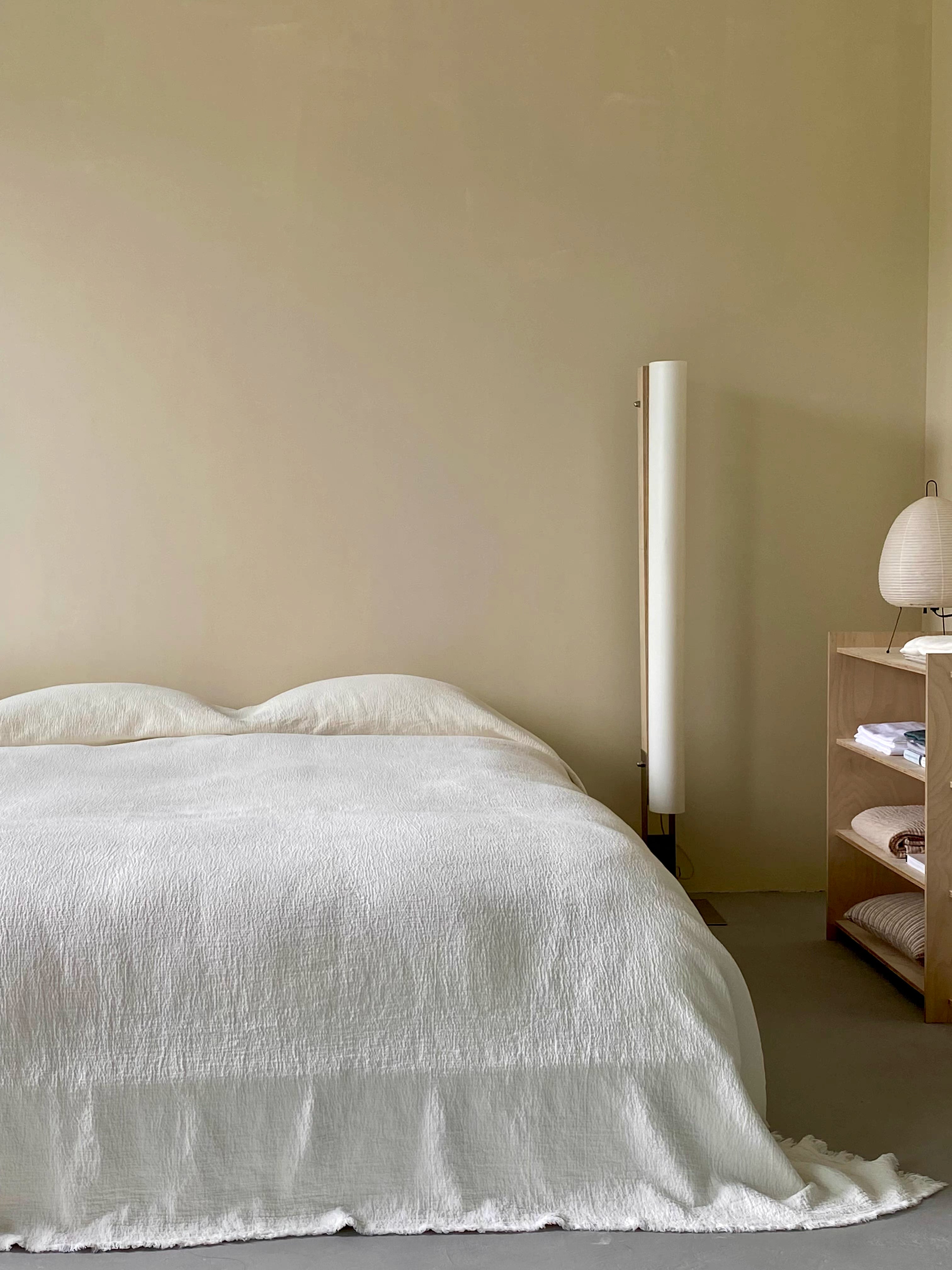 Ivory white French flax linen duvet thin quilt draped across bed in minimalist bedroom with soft breathable stonewashed linen texture and raw edge finish