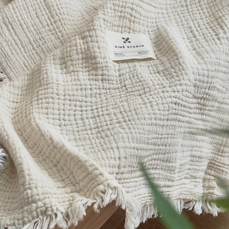 Close-up of ivory white organic cotton waffle textured throw blanket highlighting breathable gauze weave and fringe edges.