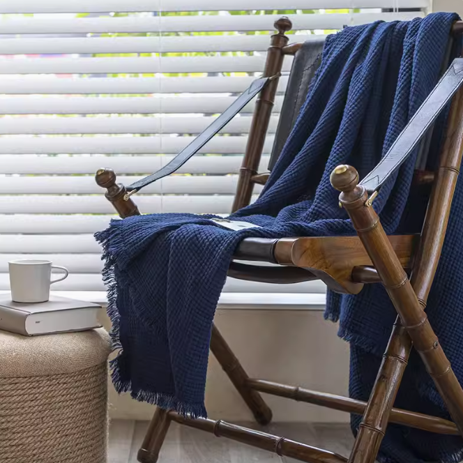 Navy blue waffle textured organic cotton fringe throw blanket draped over wooden chair in cozy living room setting.