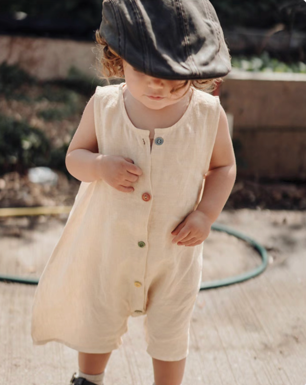 Baby wearing peach sleeveless cotton romper with button front soft breathable summer outfit lifestyle close view