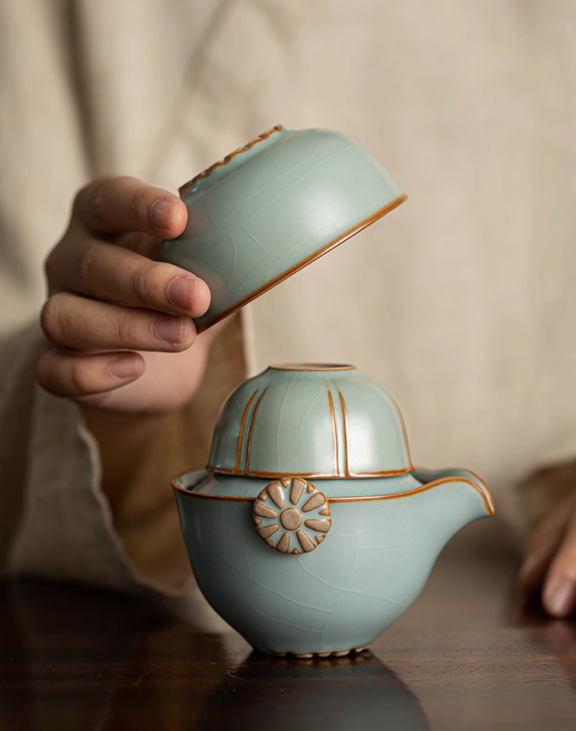 Sky blue Ru kiln ceramic teapot with stacked cups being placed on top