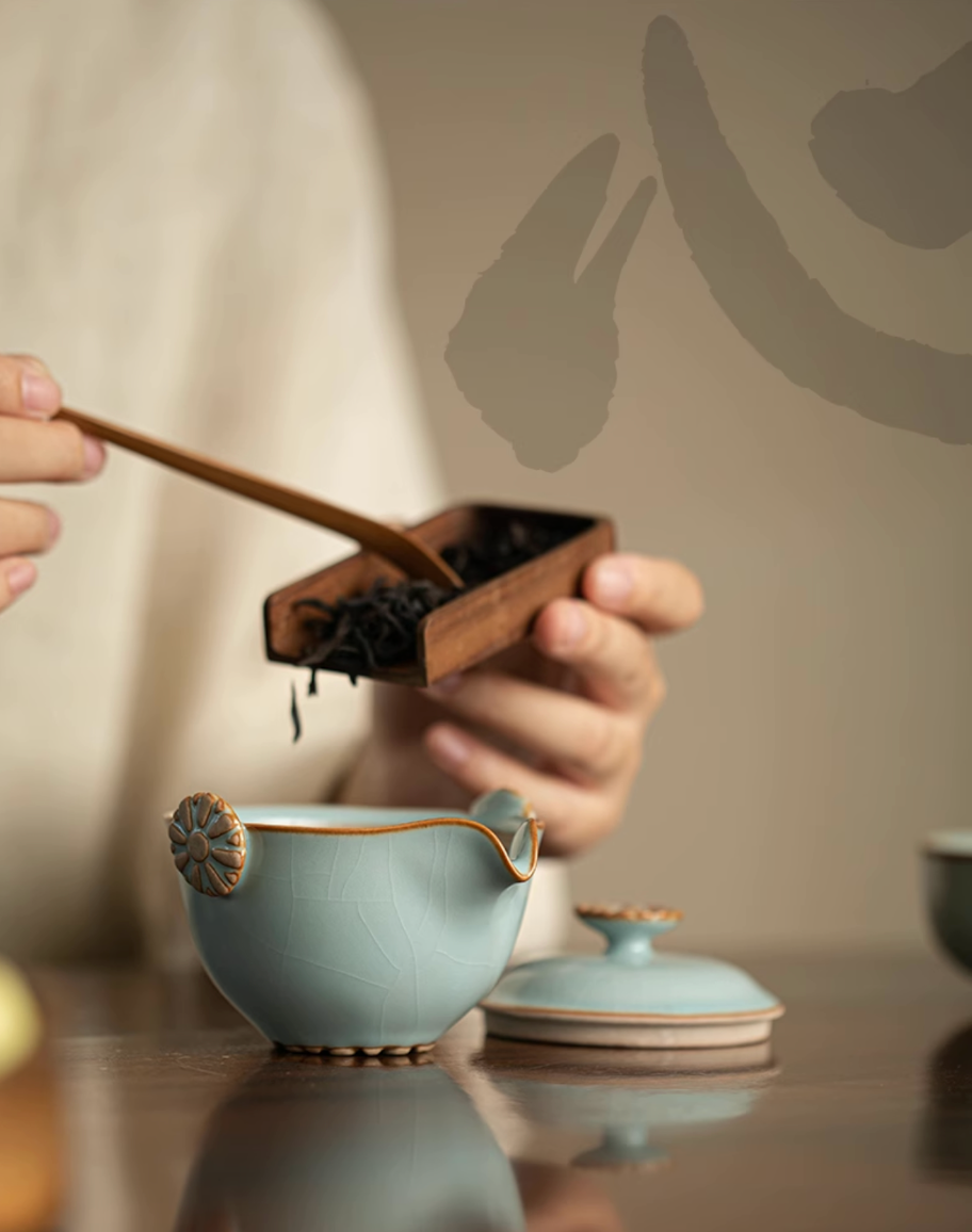 Sky blue Ru kiln ceramic teapot with lid removed while adding loose tea leaves