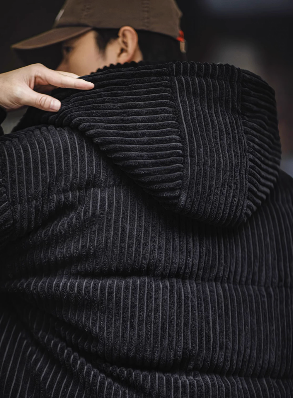Close-up of Black corduroy down jacket hood detail showing thick ribbed texture and removable hood structure