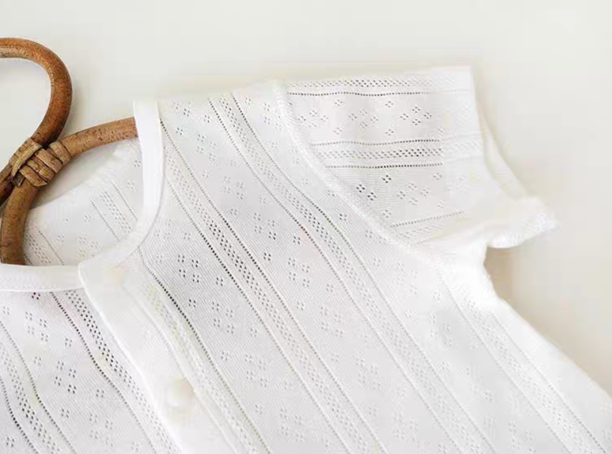 Close-up of white baby romper showing breathable eyelet knit texture and soft cotton fabric