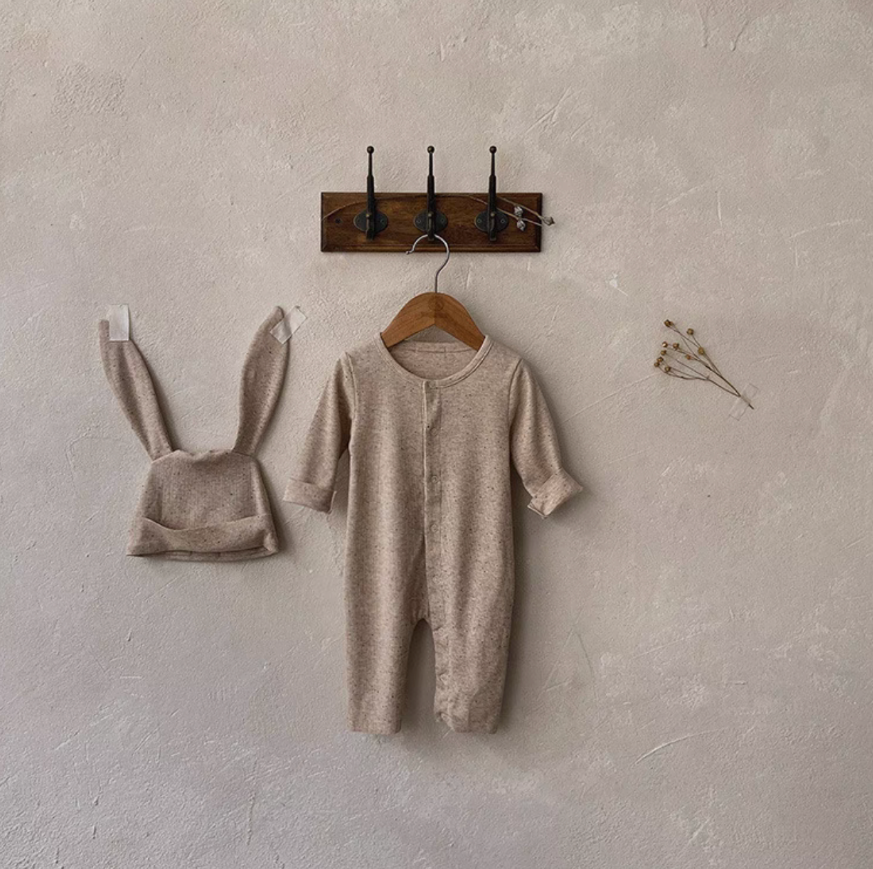 Oatmeal beige long sleeve full-length baby romper with bunny ear hat hanging on wall