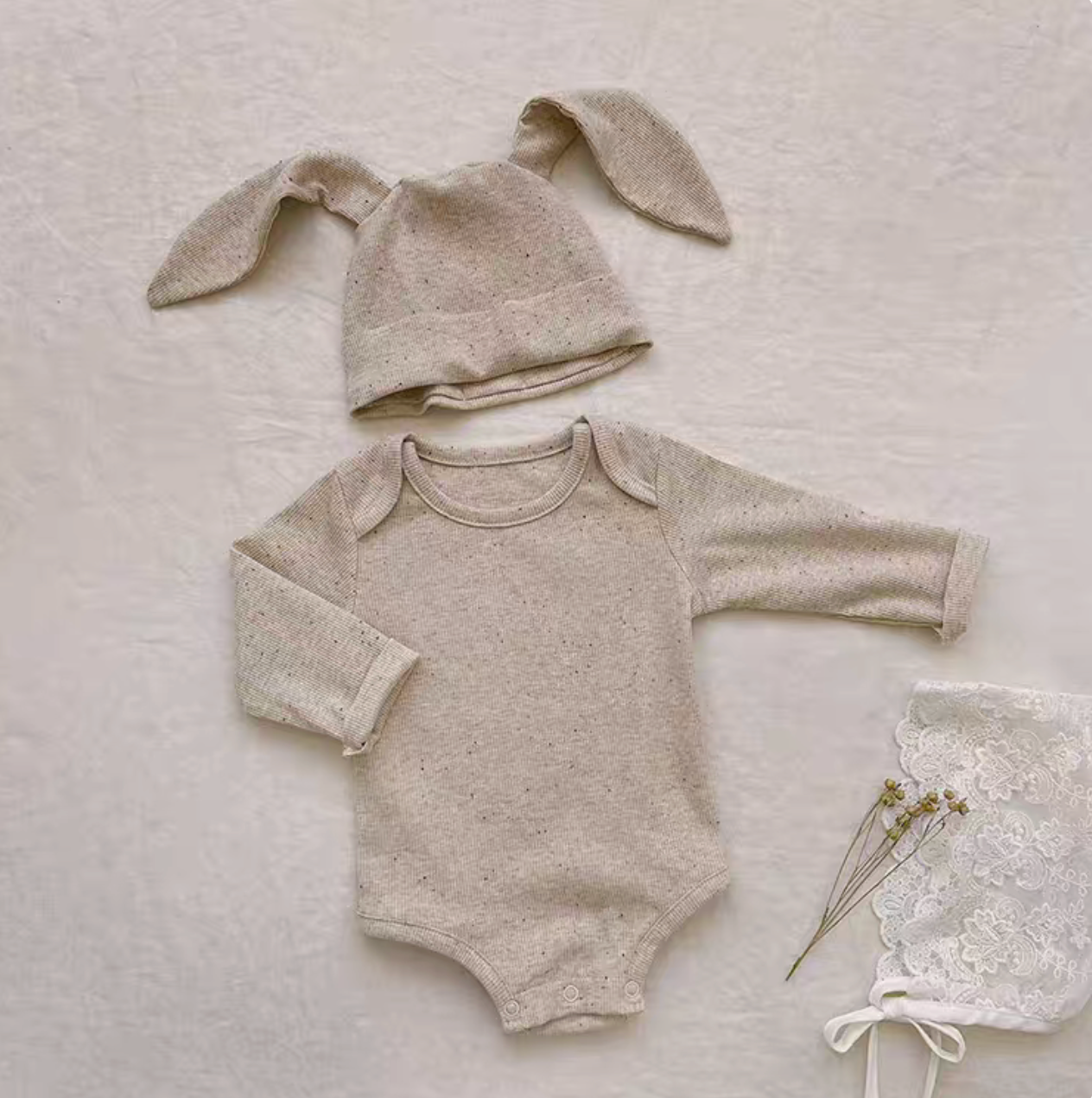 Flat lay oatmeal beige baby bodysuit with bunny ear hat showing soft cotton texture