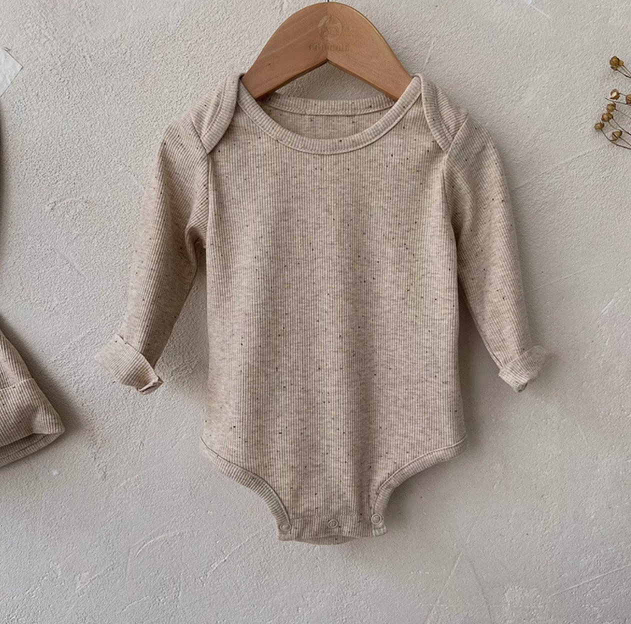 Close-up front view of oatmeal beige long sleeve baby bodysuit showing ribbed cotton fabric