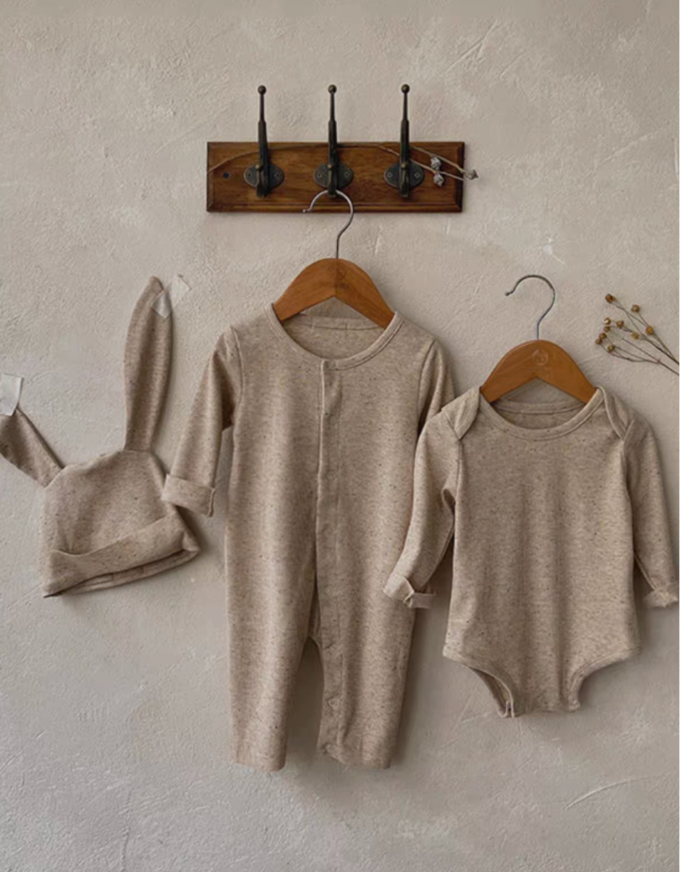 Oatmeal beige long sleeve short baby romper set with bunny ear hat hanging on wall display