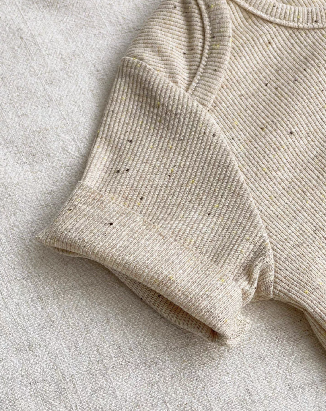 Close-up of oatmeal beige baby romper sleeve showing soft breathable cotton texture