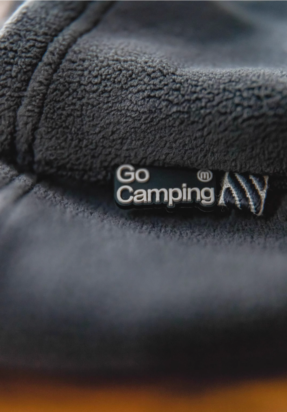 Close-up of Cozy Magic Neck-Warmer in gray showing plush fleece texture and Go Camping logo tag detail