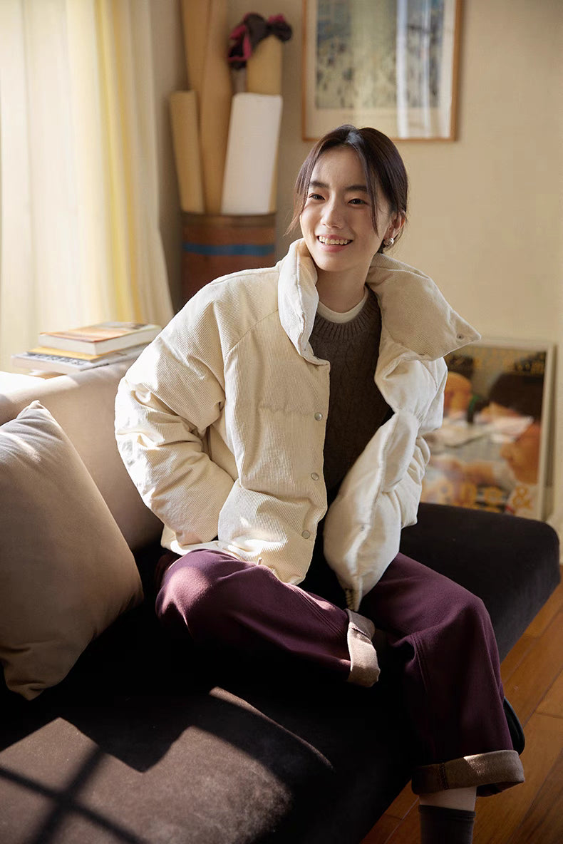 Seated lifestyle view of Cozy Quilted Corduroy Coat in off white showing relaxed fit, soft quilted fabric, and cozy winter styling