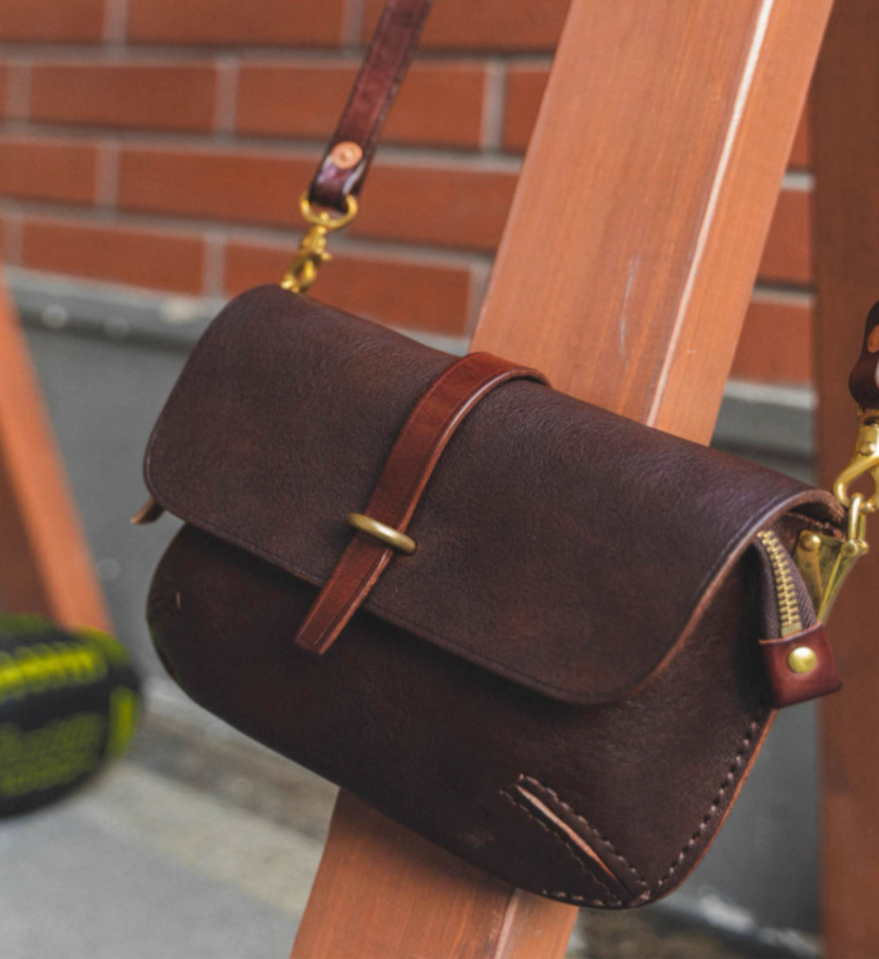 Dark espresso leather crossbody satchel resting on wooden chair outdoors