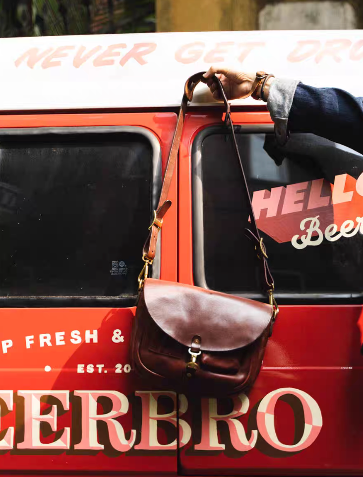 Brown Italian leather messenger bag hanging on red vintage van door