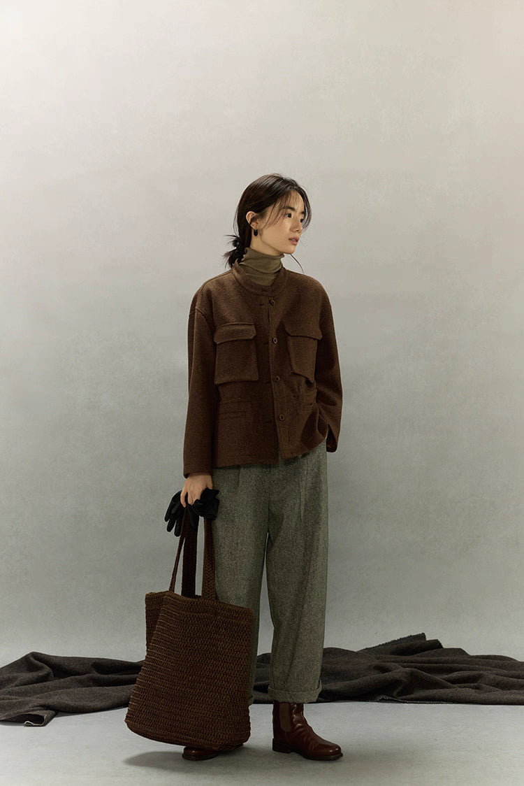 Full-length view of woman in dark coffee alpaca wool field jacket, grey pants, brown boots and knitted tote bag