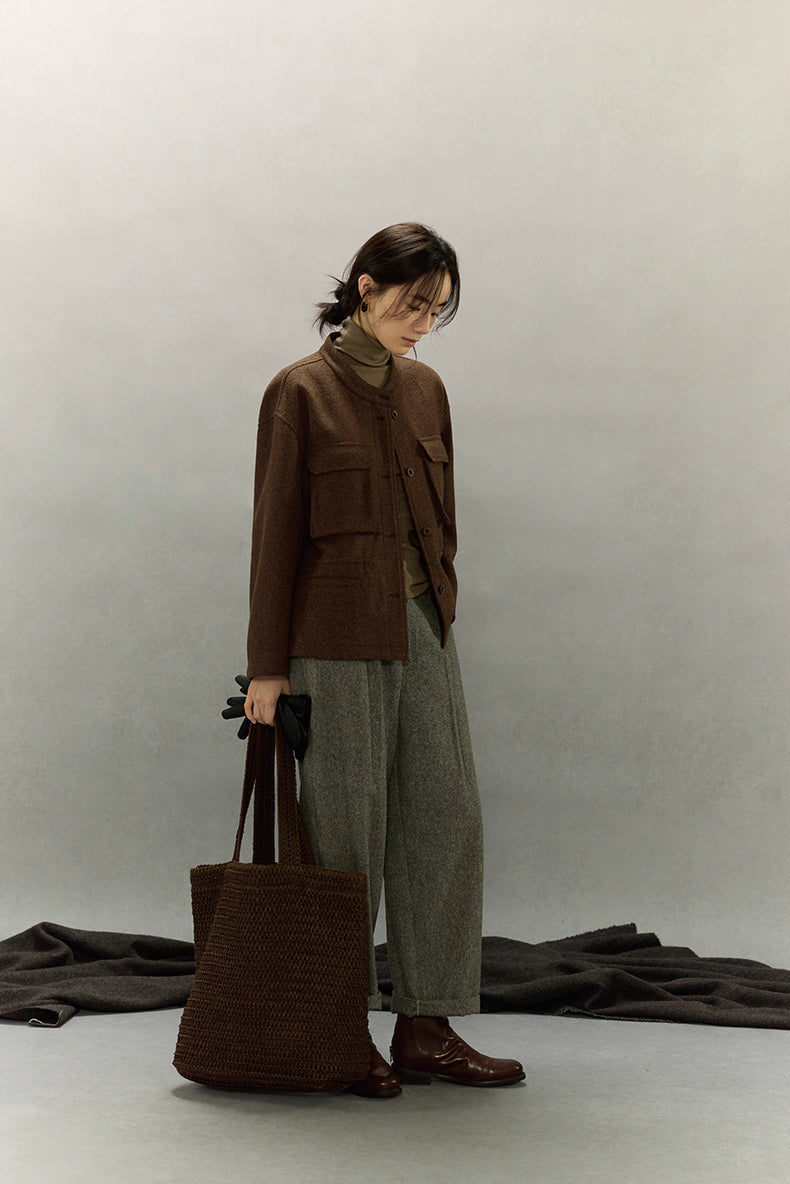 Full-body studio shot of woman looking down in dark coffee alpaca wool field jacket holding gloves and tote