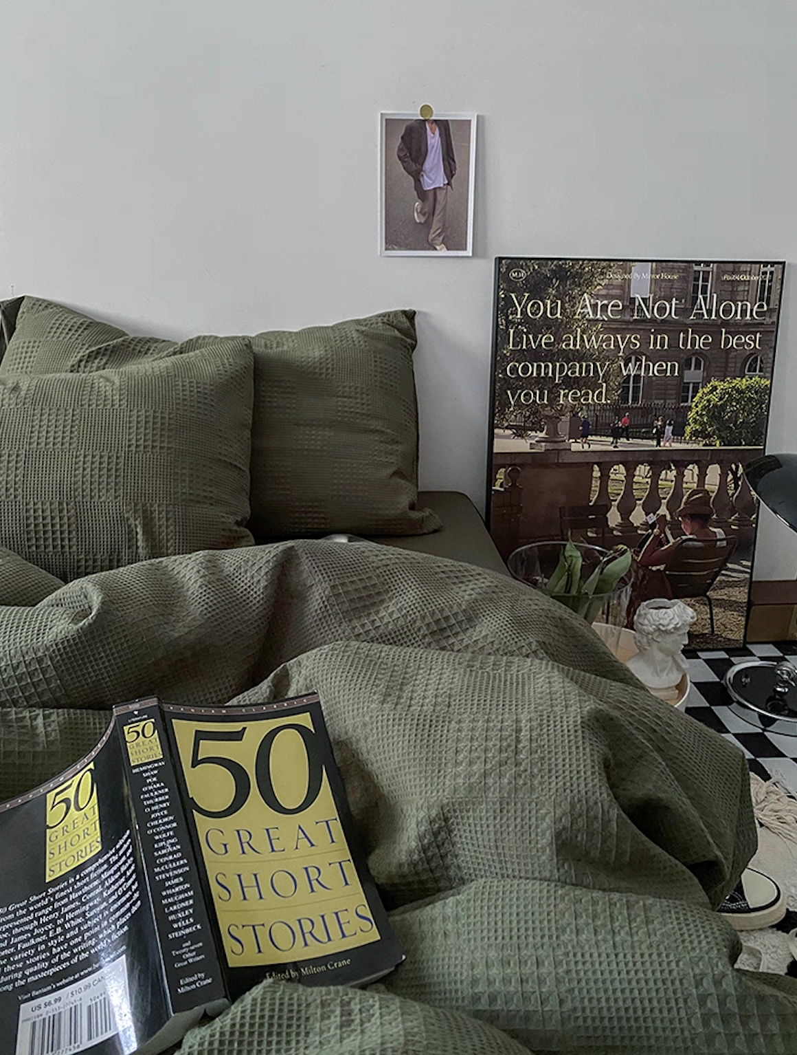 Army green diamond-waffle jacquard bedding set with pillows, book and framed artwork in a moody bedroom scene.