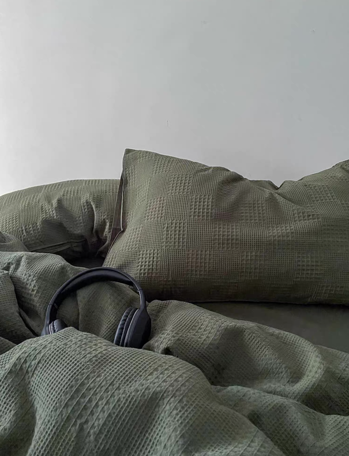 Army green waffle-weave duvet and oversized pillow; minimal bed scene with headphones for a relaxed aesthetic.