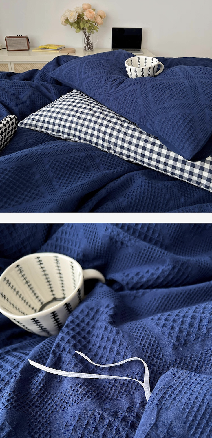Royal blue waffle-weave duvet detail with checkered pillow and ceramic cup; cozy lifestyle bedding scene.