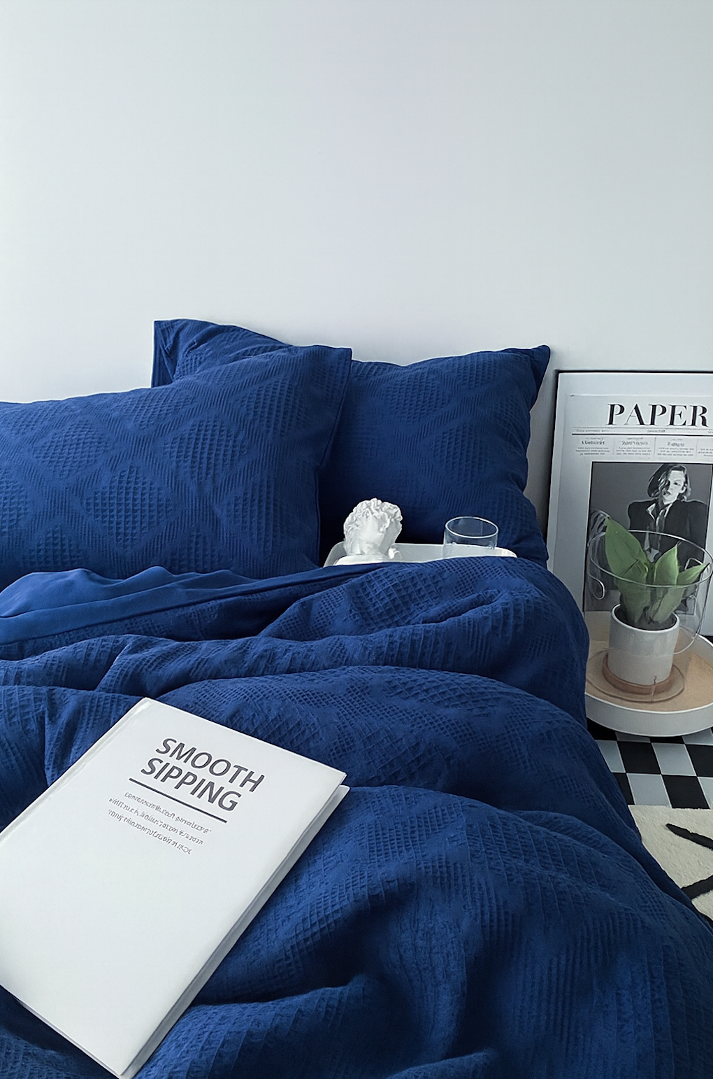 Royal blue diamond-pattern duvet and pillows with white book and decor on tray; airy, minimalist bedroom styling.