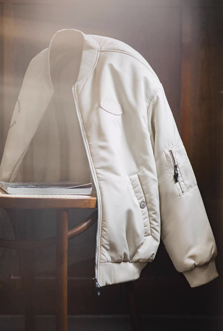Cream bomber jacket draped on chair beside magazine showing soft sheen texture
