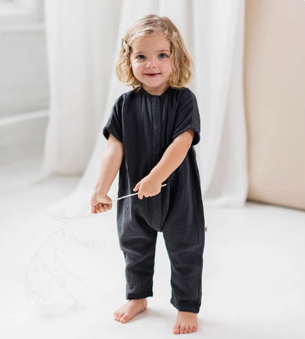 Smiling toddler wearing charcoal gray breathable cotton romper holding small branch