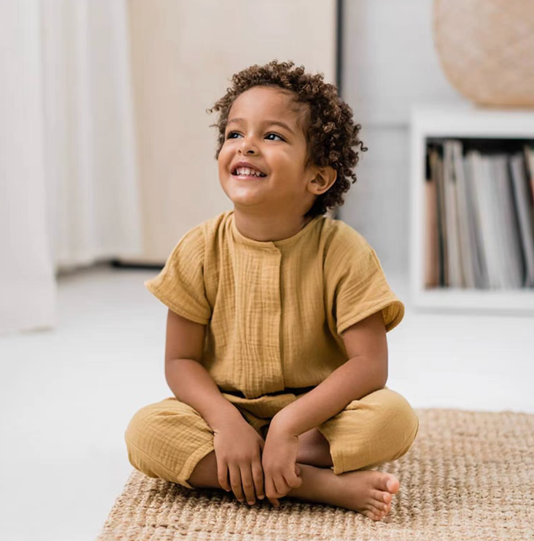 Toddler sitting and smiling wearing yellow breathable cotton romper indoors