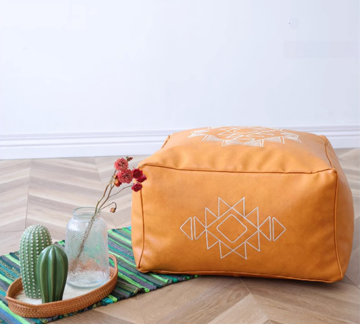 Orange yellow embroidered square bean bag sofa with white geometric pattern placed on a wooden floor with decorative vase and cactus