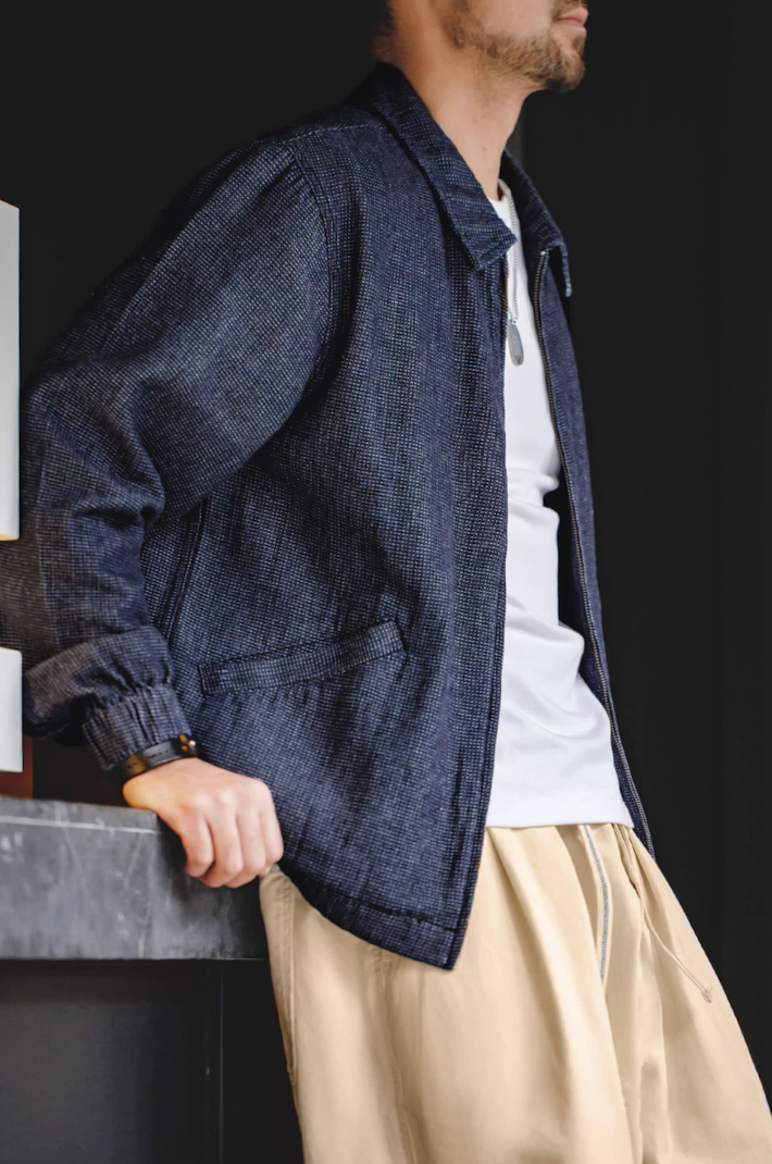 Model wearing denim coach jacket with white tee and beige pants, leaning sideways