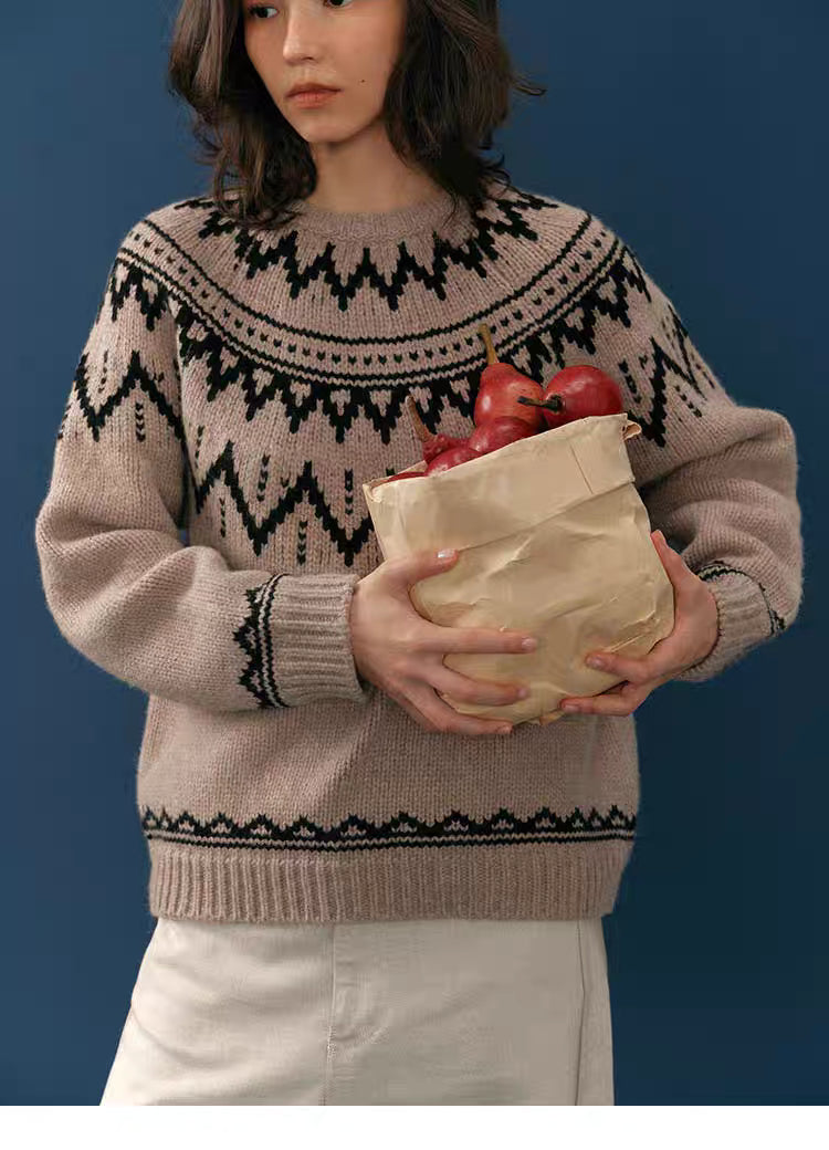 Front view of taupe and black Fair Isle merino wool sweater as the model holds a full paper bag of pears in front of a blue backdrop.