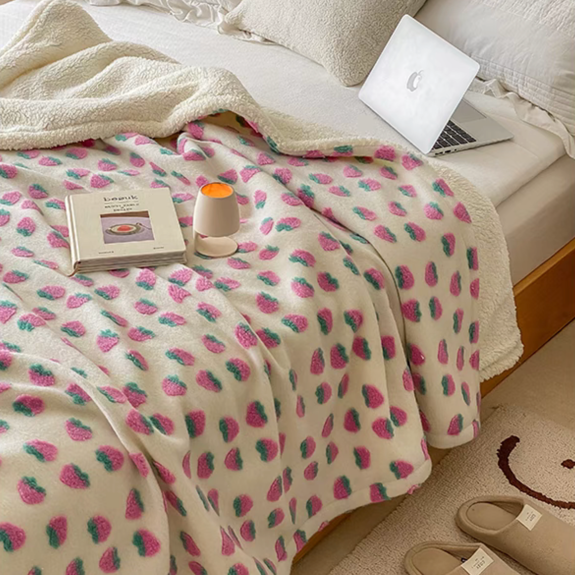 Strawberry pattern fleece throw blanket placed on bed with book and decor