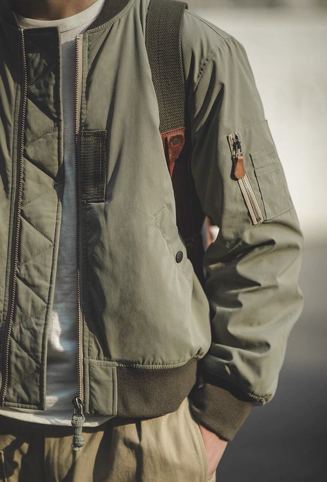 Model styling army green MA-1 bomber jacket outdoors with casual outfit.