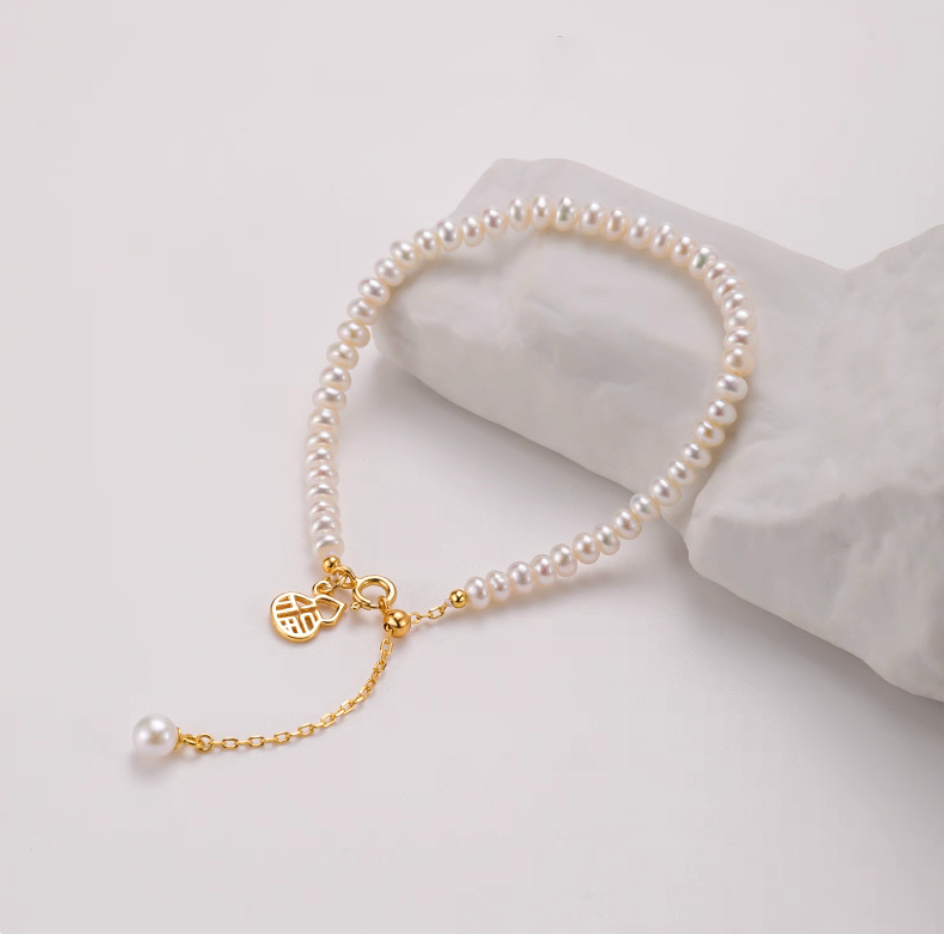 Freshwater pearl bracelet with 4–5 mm beads and gourd “Fu” charm, gold-plated sterling silver, product close-up on stone.