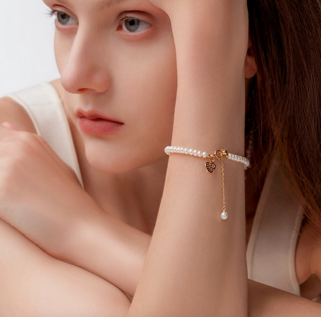 Lifestyle shot of pearl bracelet on wrist—4–5 mm pearls, gold-plated Fu good-luck charm, minimalist style.