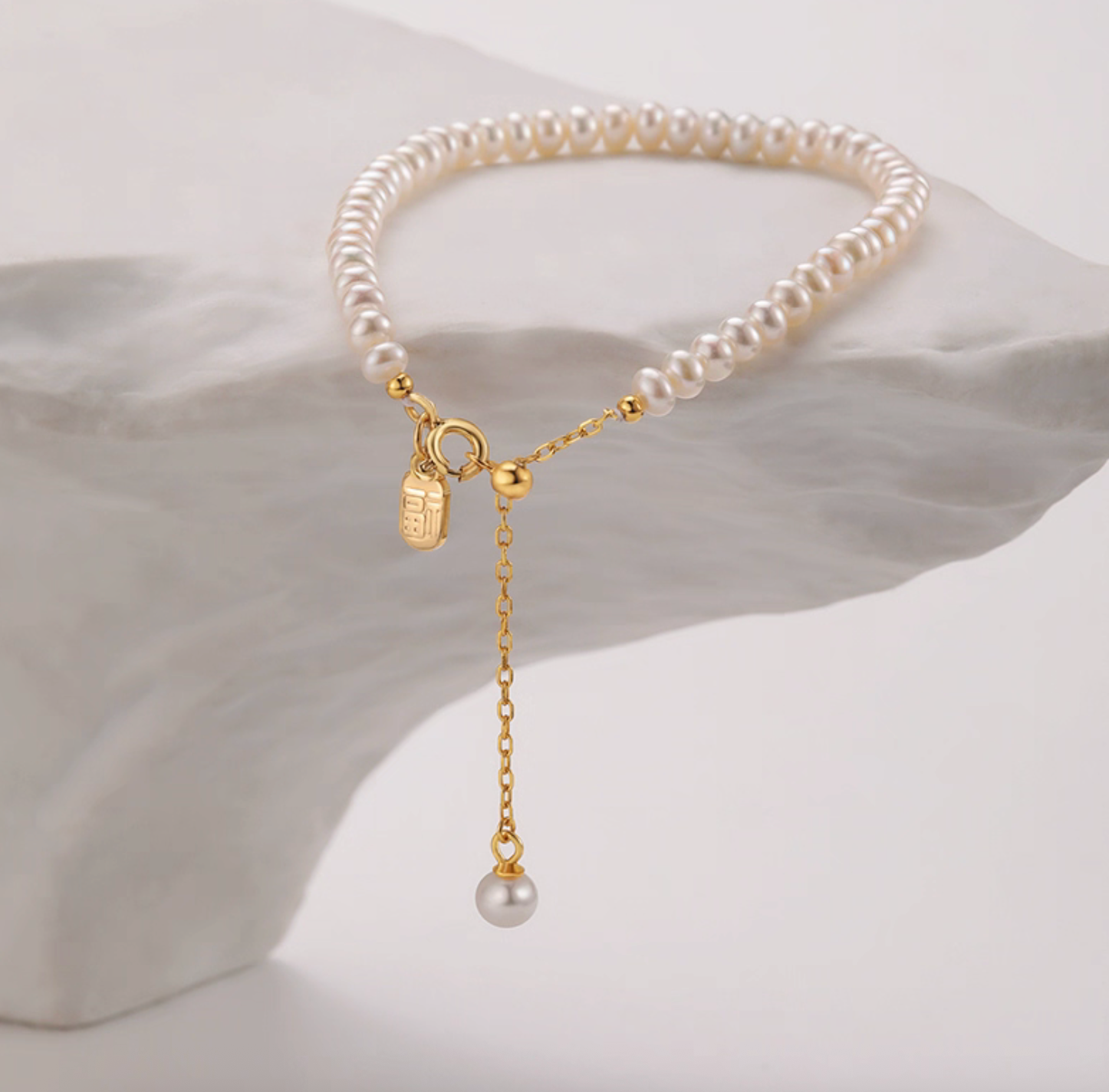 Freshwater pearl bracelet with gold-plated Fu tag charm and drop pearl, clean product image.