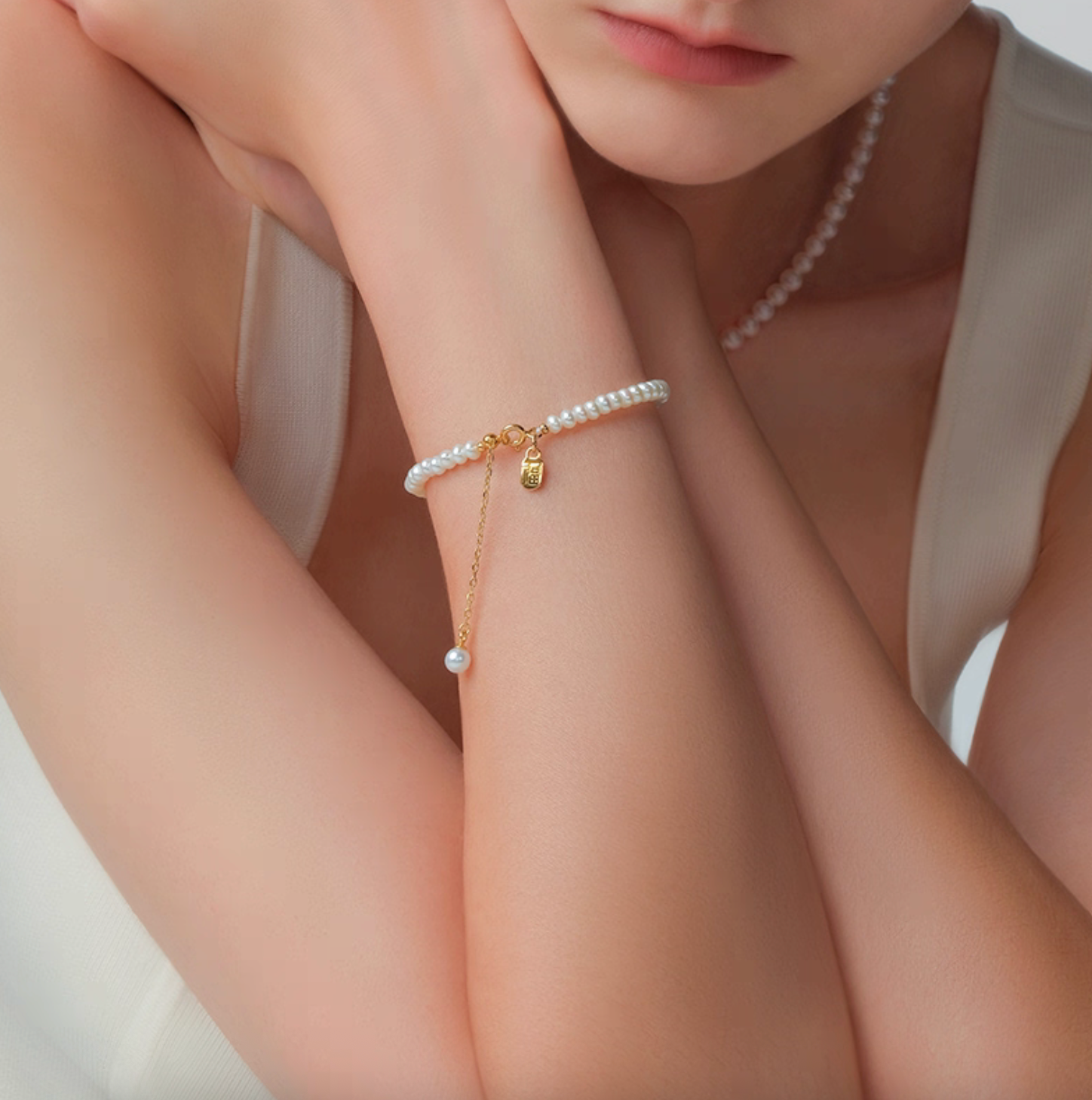 Portrait lifestyle photo showing pearl bracelet with Fu tag charm, dainty 4–5 mm pearls, gold accents.