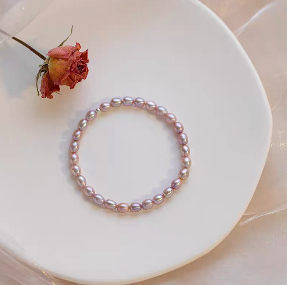 Flat lay of pinkish purple freshwater pearl stretch bracelet on plate with dried rose, highlighting soft romantic tones.