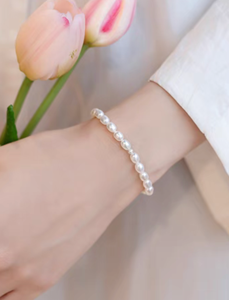 Lifestyle image of white freshwater pearl stretch bracelet worn on wrist, paired with soft neutral outfit and tulip background.