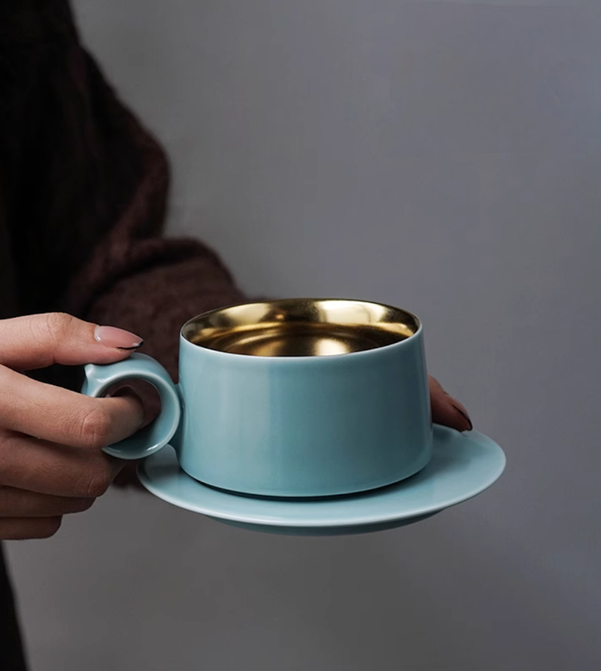 Sky Blue Gold ceramic coffee mug held in hand, showcasing ring handle grip and gold interior with Lily of the Valley engraving