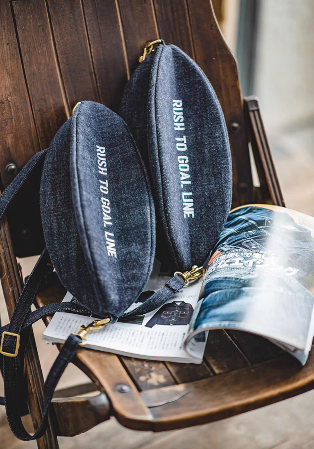 Two Goal-Line Denim Sling Crossbody Bags in denim blue displayed on chair highlighting structured silhouette contrast stitching brass clips and sporty rugby inspired design