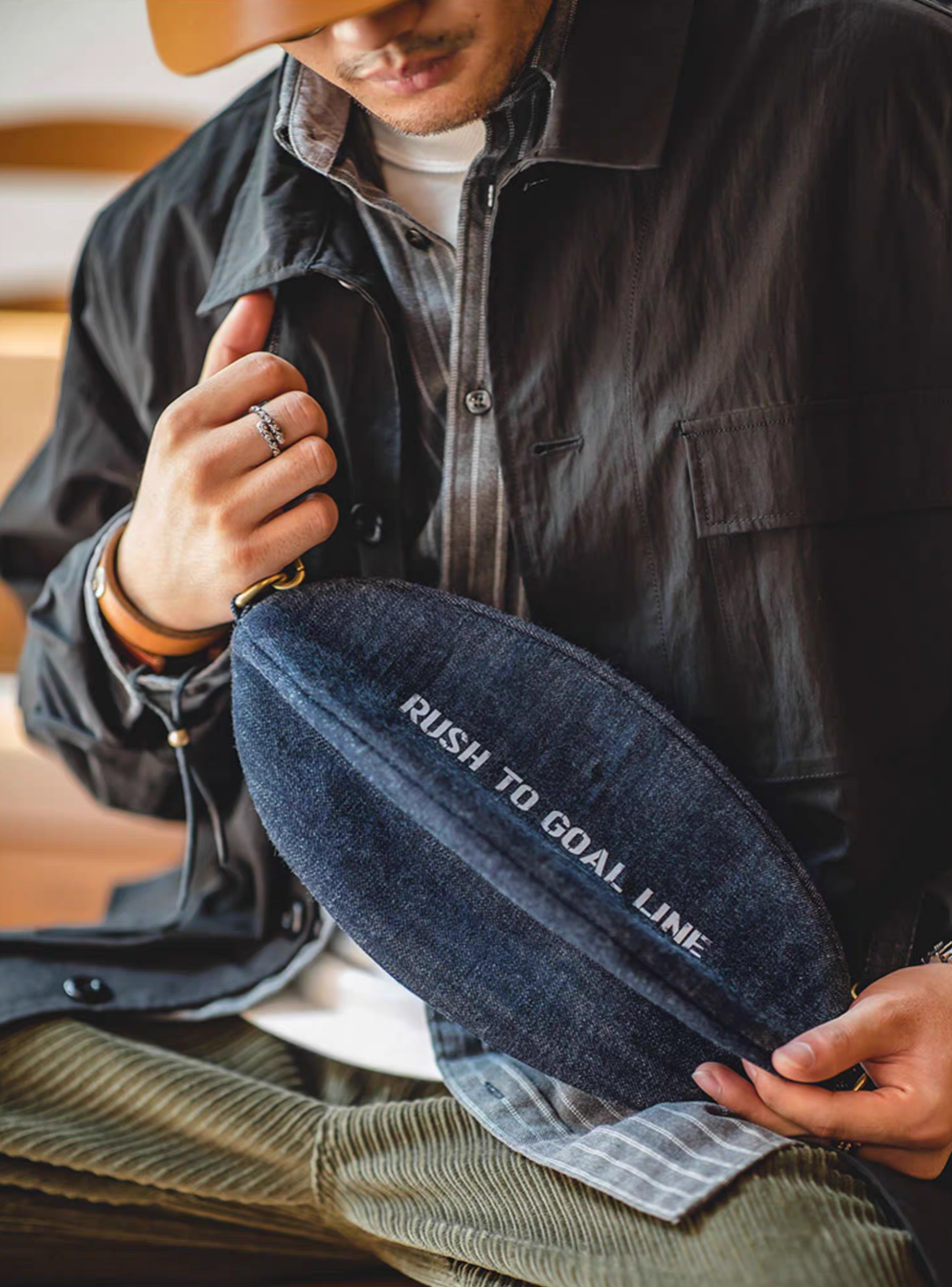 Close view of Goal-Line Denim Sling Crossbody Bag denim blue held in hand highlighting textured cotton denim construction zip closure and bold sporty typography